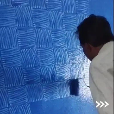 A painter demonstrates the creation of a blue basket-weave texture. This hands-on process allows for a truly custom finish, giving the wall a dynamic, fabric-like appearance that standard paint cannot replicate.