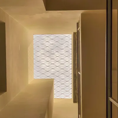 A view looking up through a light well in the Tripathy residence. The simple grill on the skylight creates a delicate, shifting pattern of shadows on the walls below, adding a layer of texture and interest.