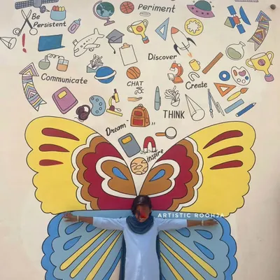 A student poses with a butterfly wing mural filled with doodles about creativity, discovery, and learning. These interactive murals serve as fun photo spots for the children.