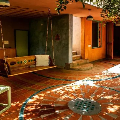 This sacred morning space in an artist's home is nestled amidst Honge trees. The design uses earthy lime plaster, terracotta floor tiles with a custom inlay, and a traditional jhula to create a shaded outdoor living area that feels both grounded and poetic.