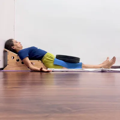 Supported Savasana on a Simhasana Box with weights on the thighs. This setup gently arches the upper back to open the chest, deepens the breath, and grounds the body to calm the nervous system.