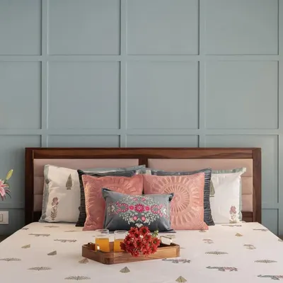 The master bed in this room is set against a beautiful pastel blue wall with classic square paneling. We added small, adjustable reading lights on either side, creating a perfect blend of traditional charm and modern functionality.