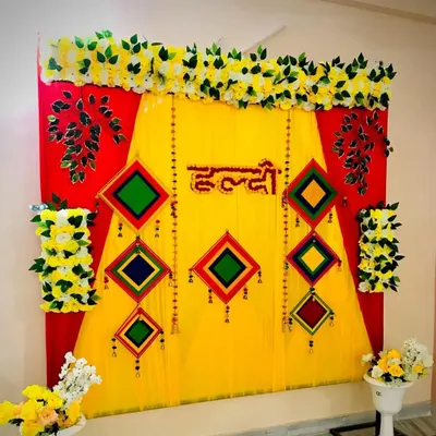 This is a traditional Haldi backdrop I set up at a client's home. It combines bright yellow and red drapes, topped with artificial marigold garlands and decorated with colorful hanging tassels for a truly festive look.