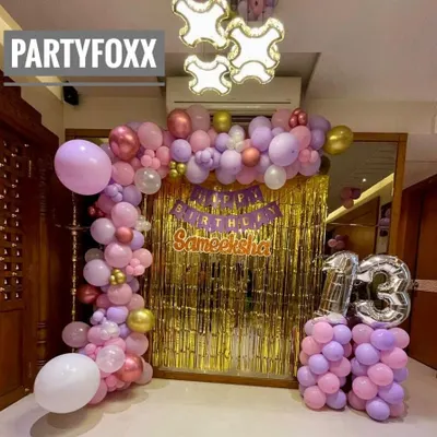 A beautiful at-home 13th birthday decoration for Sameeksha. The setup includes a gold sequin backdrop and a pink and purple balloon arch with silver number balloons.