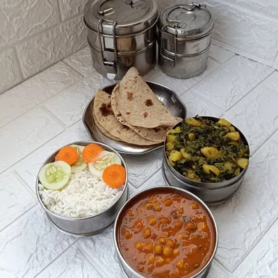A standard lunch or dinner tiffin, featuring two soft rotis, steamed rice, wholesome aloo methi sabzi, a comforting mutter gravy, and a fresh salad. It's a complete meal designed to be both nutritious and satisfying.