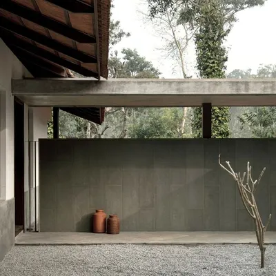 The entrance to the Polibetta Farmhouse, where a minimalist design meets the lush Coorg landscape. A long Kota stone-clad wall guides visitors and frames the entry court, hinting at the views beyond.