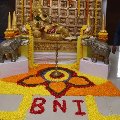 A traditional Ganesha installation for a BNI corporate meet. The decor includes a large floral rangoli on the floor spelling out "BNI," seamlessly integrating the company's identity into the festive design.