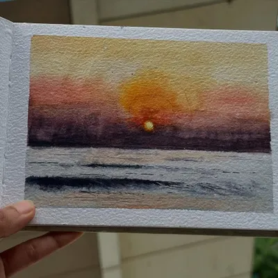 A small watercolor study of a sunset over the sea, painted in my sketchbook. I focused on blending the warm yellows and oranges of the sun with the cool purples of the water to capture that fleeting moment of the day.