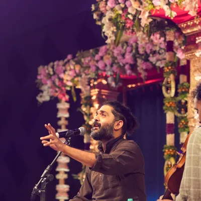 An energetic shot of singer Sid Sriram performing live on stage at the ISKCON Whitefield Janmashtami event, capturing his passion and the beautiful floral stage decor.