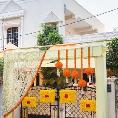 A beautifully decorated entrance sets the stage for the entire wedding. For this home, we adorned the main gate with bright orange marigold tassels and floral panels, complemented by delicate white flower strings. This creates a warm, traditional, and festive welcome for all your guests.