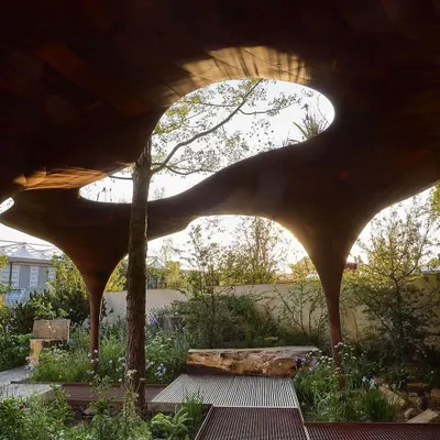 This is an example of a highly artistic, custom-fabricated pergola. The organic, curved cutouts in the wooden canopy allow natural light to filter through while creating a unique sculptural statement in the garden.