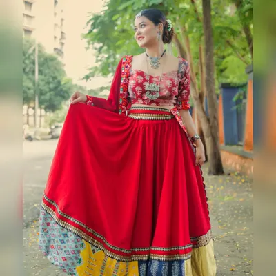 A full-length shot of a model in a vibrant red ghagra choli, taken outdoors on a city street. The image captures the flow of the skirt and the beautiful, multi-colored border.