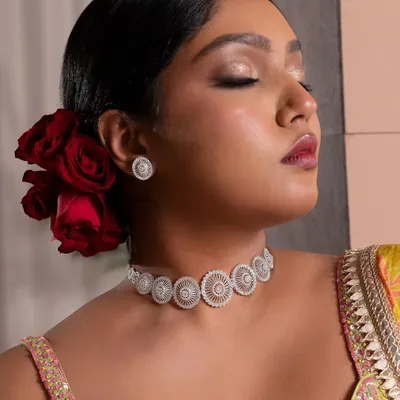 A high-fashion look for a jewellery campaign, inspired by a "desi Frida Kahlo" mood. The makeup is centered around a bold, berry-stained lip and glowing skin, with hair styled into a classic bun adorned with deep red roses for a dramatic and artistic feel.