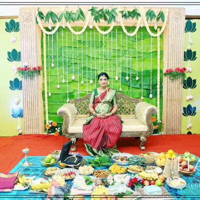 A beautiful stage setup for a Seemantham (baby shower) ceremony. The design features a backdrop of banana leaves and side panels with traditional lotus block prints, creating a natural and auspicious setting for the mother-to-be.
