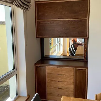 The finished drinks cabinet installed in the client's home. The design includes an upper cabinet for glassware and cookbooks, a walnut-framed mirror, and a lower unit with custom drawers and storage.