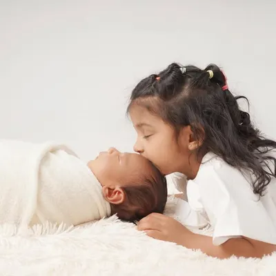 A touching moment of sibling love as a big sister gently kisses her newborn sibling's forehead.