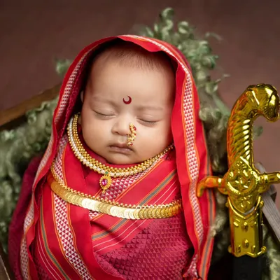 A beautiful portrait of a newborn as Rajmata Jijabai, complete with a traditional red saree wrap, gold coin necklace, and a miniature sword. I focus on getting these details just right while the baby sleeps soundly.