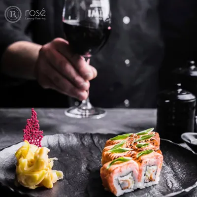 We are ready to elevate your special occasions with our premium catering services. This image of a sommelier with a glass of red wine and a plate of sushi captures the sophisticated dining experience we offer.