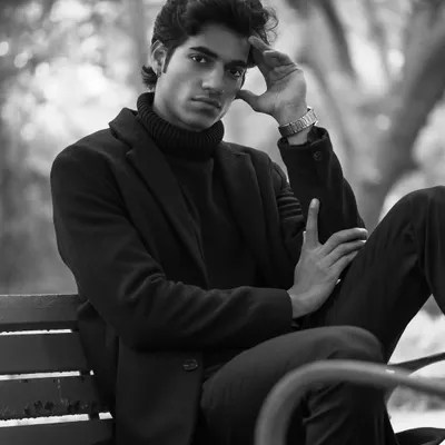 This black and white portrait, taken on a park bench, has a thoughtful and cinematic feel. The monochrome treatment emphasizes the texture of the clothing and the model's contemplative expression.
