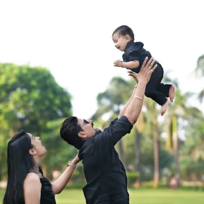 A classic, joyful family moment captured outdoors. A father lifts his child high in the air while the mother looks on, creating a dynamic and love-filled portrait.