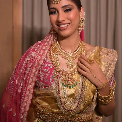 A stunning South Indian bridal look featuring a golden Kanjeevaram saree and layers of traditional temple jewelry. The makeup is soft glam, with defined eyes and radiant skin to complement the richness of her attire.
