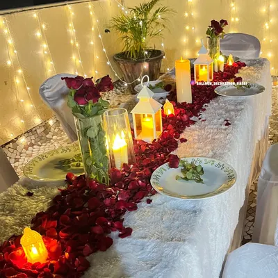 A close-up of the romantic table setting for a candlelight dinner. The table runner is made of hundreds of fresh red rose petals, interspersed with candles in glass holders and decorative lanterns.