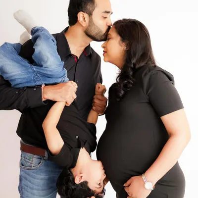 A playful and heartwarming family portrait. This photo perfectly captures the fun and chaos of family life as the parents-to-be share a laugh with their energetic son.