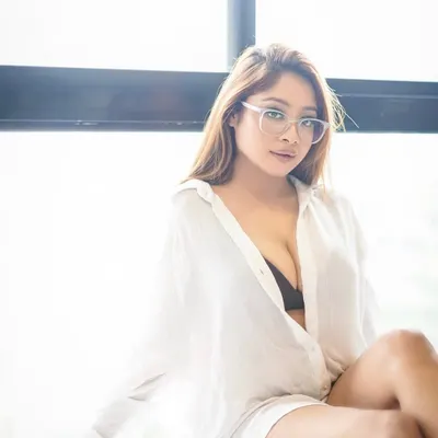 A soft, naturally lit portrait of a model in a simple white shirt. The glasses add a touch of character, creating a relatable and stylish lifestyle image.