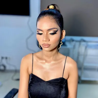 A close-up of a dramatic, high-fashion look. The sleek high ponytail is accented with a gold accessory, and the sharp, graphic winged liner makes a bold statement.