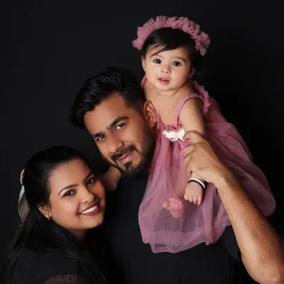 A classic family portrait against a simple black background. The focus is entirely on the family's connection, with the father holding his daughter on his shoulders.