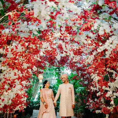 A romantic portrait of the couple framed by a stunning red and white floral arch. The way they look at each other captures the magic of the moment.