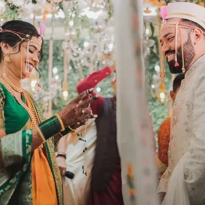 A beautiful moment from a traditional Marathi wedding, capturing the playful interaction between the bride in her Nauvari saree and the groom.