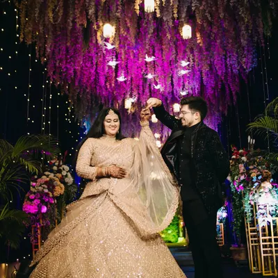 A magical first dance under a ceiling of cascading purple flowers and hanging lanterns. This shot captures the fairytale ambiance of a grand engagement reception, highlighting the couple's joy and the stunning decor.