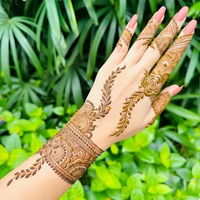This elegant design features a leafy vine pattern that trails up the finger, connected to a beautiful wrist cuff. It's a perfect example of a modern and chic party mehandi.