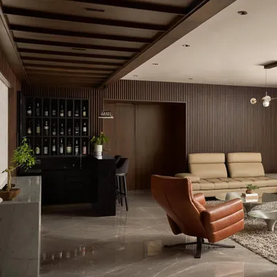 An overview of the Project Acropolis living room and bar area. The design uses a dark palette with fluted wood walls, leather furniture, and marble floors to create a sophisticated and cohesive environment.