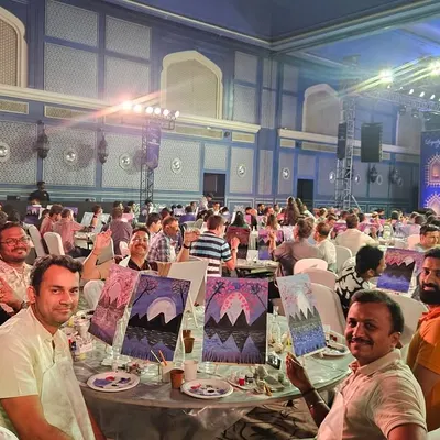 A table of happy employees from a corporate conference, proudly showing off their mountain landscape paintings. It's amazing to see how a little paint can spark so much conversation and teamwork.