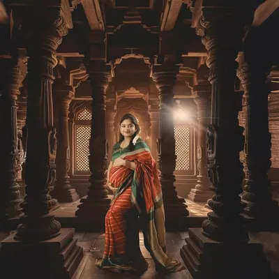 A powerful portrait set within a grand, traditional temple-style hall. The intricate pillars and dramatic lighting create a sense of heritage and divine grace for this maternity photo.