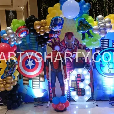 An action-packed Avengers photo booth with a city skyline backdrop, character cutouts of Iron Man, Captain America, and Hulk, and a light-up number '3'.