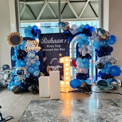 I designed this detailed outer space theme for a first birthday party. The backdrop features a full balloon arch, astronaut and planet cutouts, a personalized sign for "Ruhaan's First Trip Around the Sun," and a bright, light-up number '1'.
