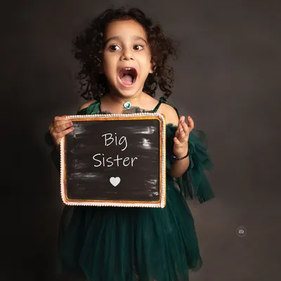 The pure excitement of becoming a big sister! Her expressive face says it all in this fun and memorable announcement photo.