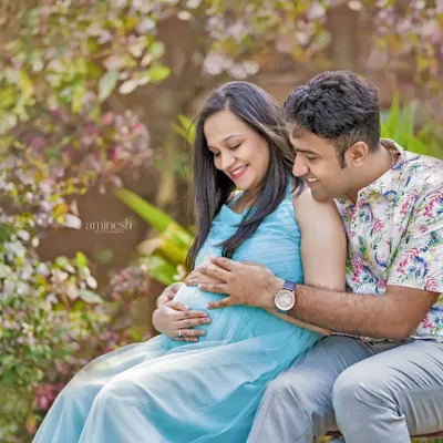An expecting couple shares an intimate moment in a lush garden setting. This outdoor maternity portrait uses natural light to create a soft and romantic feel.