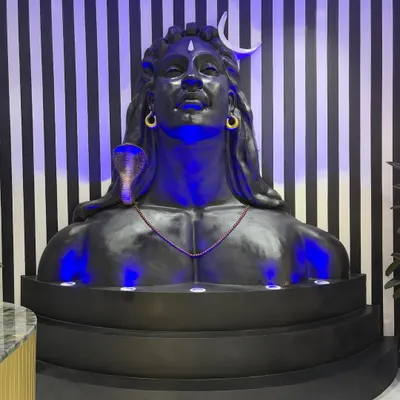 The final Adiyogi-inspired sculpture installed in the office lobby, illuminated with dramatic blue uplighting. The piece is set against a bold striped wall, creating a modern shrine that commands attention.