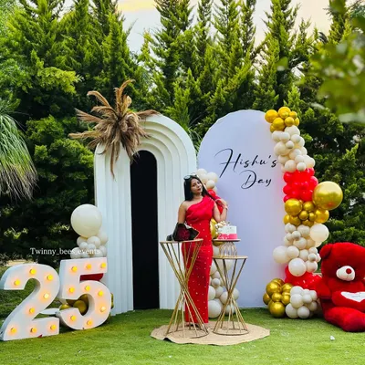 A stunning outdoor setup for Hishu's 25th birthday. We used modern arched backdrops, a vibrant red, white, and gold balloon arrangement, and large marquee numbers to create a chic and celebratory photo zone.