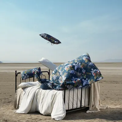 A surreal composition for a home fashions campaign, featuring a bed in the middle of a desert with linens flying in the air. This image breaks from traditional interior photography to create a sense of freedom and imagination.
