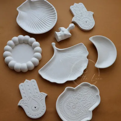 A flat lay of my diverse collection of eco-resin trinket trays. You can see the different shapes I offer, including seashells, hamsa hands, moons, and ginkgo leaves.