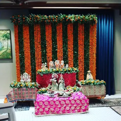 This is a traditional decoration for a home temple during Janmashtami or Ganesh Chaturthi. We created a backdrop of orange marigold and green leaf strings, providing a vibrant setting for the deities.