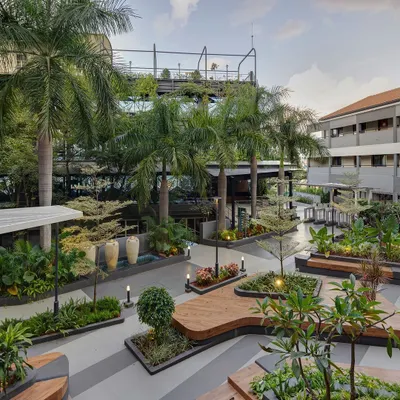 An aerial view of the completed landscape at Atria University. The design features organically shaped wooden decks that double as seating, surrounded by lush planters and mature palm trees, creating a vibrant campus hub.
