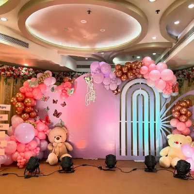 A gorgeous butterfly-themed baby shower, featuring a large backdrop with butterfly wing cutouts and a "Oh Baby" sign. The decor is a beautiful mix of pink and rose gold balloons, with two teddy bears adding a touch of cuddly sweetness.