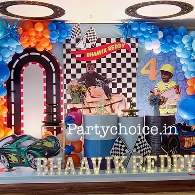 A thrilling Hot Wheels car theme for a 4th birthday. This setup features a checkered flag backdrop, a racetrack arch, car cutouts, and custom photos of the birthday boy incorporated into the design.