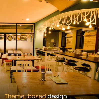 This wide shot of the Sattviko Idea Café showcases the theme-based design. The space is organized into different zones, including a long community table and smaller group tables, with unique overhead lighting to foster an environment where ideas can take shape.